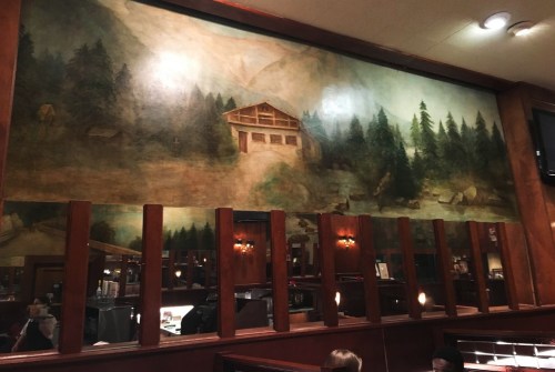A mural depicting a serene mountain landscape with a cabin and trees, set in a cozy restaurant interior.