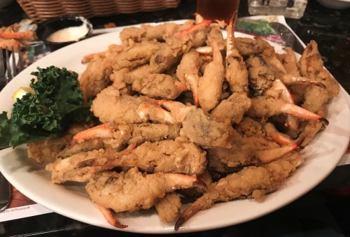 A large plate of golden-brown fried crab claws, garnished with a lemon wedge and a piece of kale.