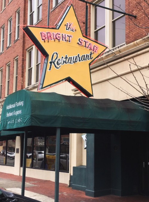 Sign for "The Bright Star Restaurant" featuring a large yellow star, with a green awning and brick building backdrop.