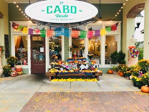 Colorful Mexican restaurant entrance decorated with flowers, pumpkins, and papel picado banners for a festive atmosphere.