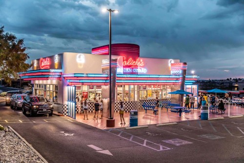 A retro ice cream shop with neon lights, surrounded by cars and people enjoying the outdoor seating.