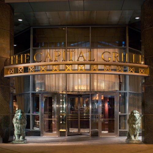 Entrance of The Capital Grille, featuring large glass doors and two lion statues flanking the entrance.