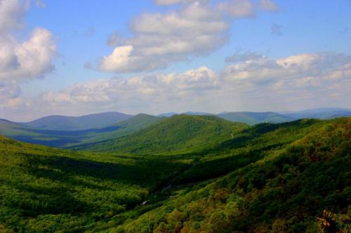 Lush green mountains under a blue sky with fluffy clouds, showcasing a serene and expansive landscape.