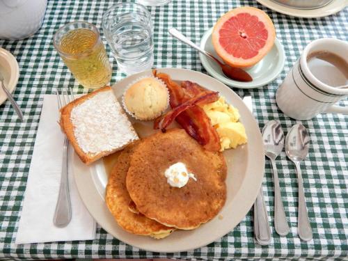 A breakfast plate with pancakes, bacon, scrambled eggs, toast, a muffin, grapefruit, and drinks on a checkered tablecloth.
