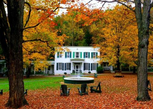 A charming white building surrounded by vibrant autumn foliage and a circular fountain in a serene outdoor setting.