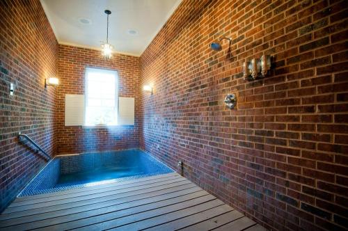 A modern bathroom with exposed brick walls, a window, and a small pool area with wooden flooring.