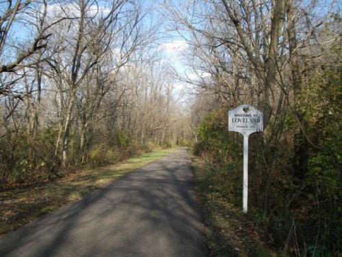 A tree-lined path with a sign reading "Welcome to Loveland" on the side, under a partly cloudy sky.