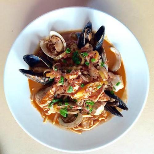 A bowl of seafood pasta featuring clams, mussels, and a rich tomato sauce, garnished with green onions.