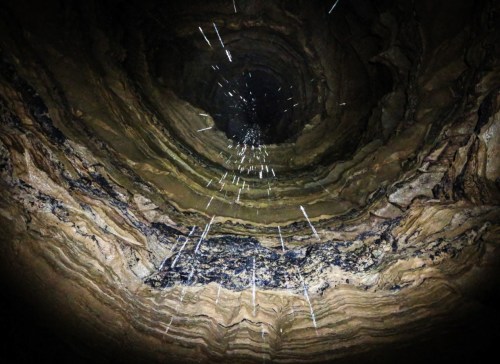 A deep, circular well with textured, layered walls and water droplets cascading down into darkness.