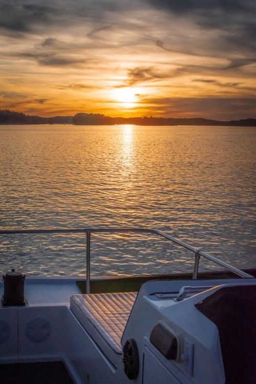 A serene sunset over calm waters, viewed from a boat with a deck in the foreground.
