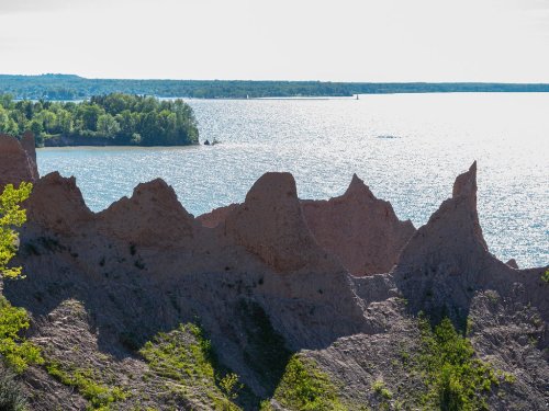 A scenic view of jagged rock formations against a shimmering lake and lush green trees in the background.