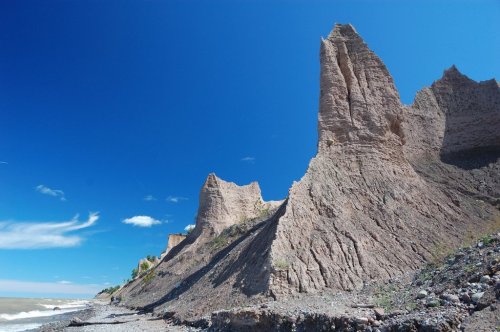 A rugged coastline with towering cliffs under a clear blue sky and gentle waves lapping at the shore.
