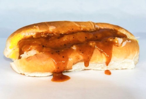A hot dog in a bun topped with a rich, brown sauce and a sprinkle of black pepper.
