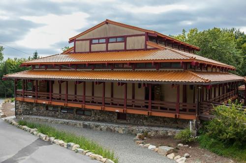 A large, multi-level building with a red roof and wooden accents, surrounded by greenery and a gravel path.