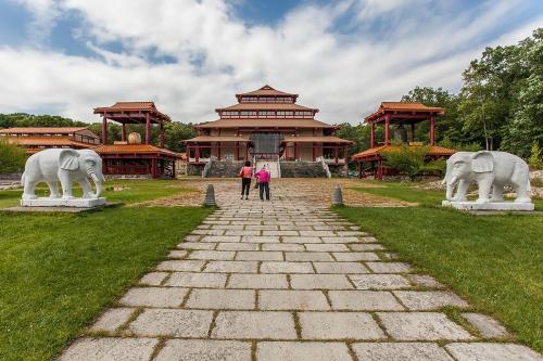 Two people stand on a stone path leading to a large Asian-style building, flanked by stone elephant sculptures.