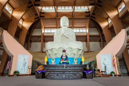A large Buddha statue sits in a wooden temple, with smaller figures and decorative elements in the foreground.