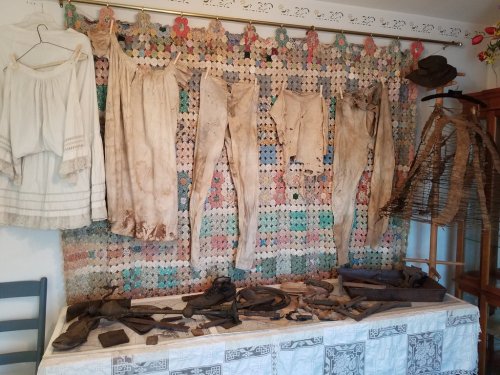 A display of vintage clothing and accessories hanging on a colorful crocheted backdrop, with various items on a table below.