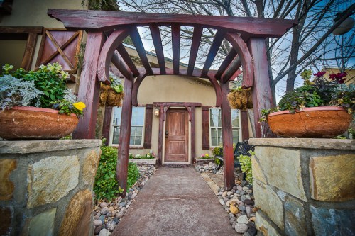 A charming entrance with a wooden arch, potted plants, and a stone pathway leading to a welcoming door.