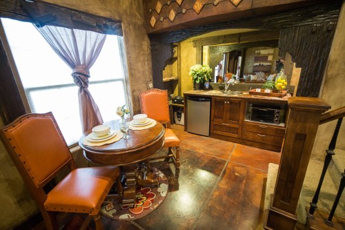Cozy dining area with a round table, two orange chairs, and a kitchenette featuring a mini fridge and decor.