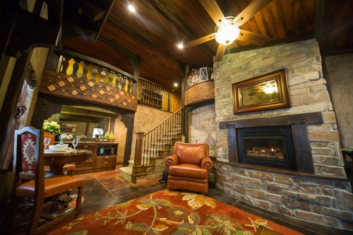 Cozy living room with a stone fireplace, wooden beams, and a leather armchair, featuring warm lighting and rustic decor.