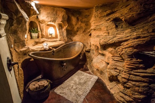 A rustic bathroom featuring a copper bathtub surrounded by natural stone walls and soft lighting.