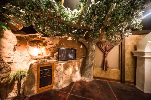 Cozy room featuring a large artificial tree, stone walls, a TV, and warm lighting for a natural ambiance.