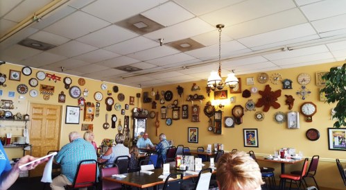 A cozy restaurant interior with colorful walls adorned with various clocks and decorative plates, featuring diners at tables.