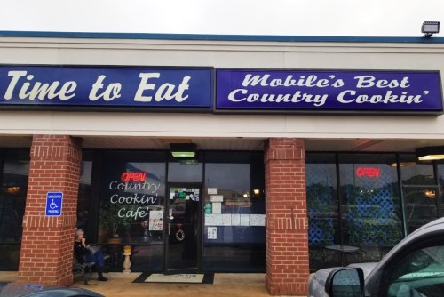 A restaurant exterior with a sign reading "Time to Eat" and "Mobile's Best Country Cookin'," featuring an open sign.