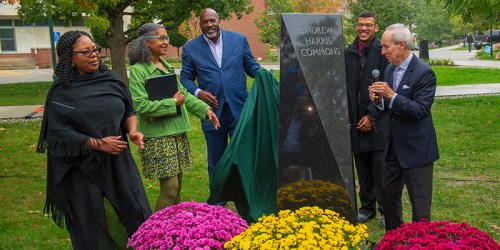 A group of people unveil a monument at a ceremony, surrounded by colorful flowers and greenery.