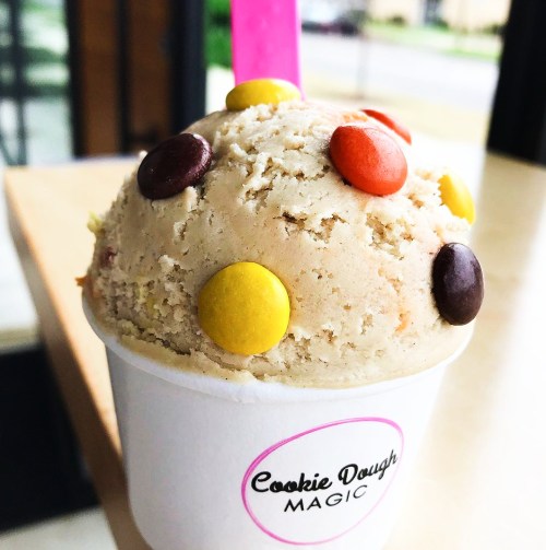 A cup of cookie dough ice cream topped with colorful candy pieces, sitting on a table.
