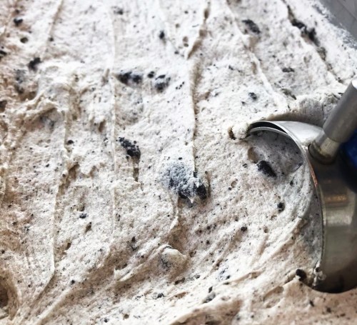Close-up of creamy, textured ice cream with cookie pieces, featuring a metal scoop resting on top.