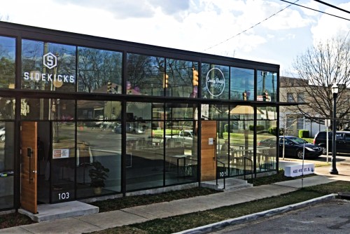 Modern glass storefront featuring "Sidekicks" and "Luna Bread" signs, with a clear view of the street and parked cars.