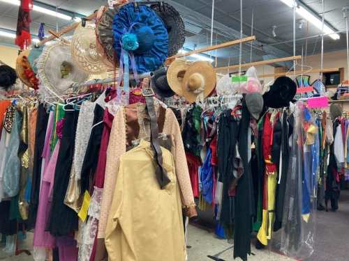A colorful assortment of costumes and hats hanging on racks in a costume shop.