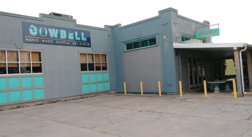 Exterior of a restaurant named "Cowbell," featuring a blue-gray facade and colorful signage.