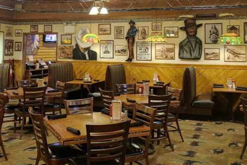Cozy restaurant interior with wooden tables, chairs, and vintage decor on the walls, including framed pictures and lamps.