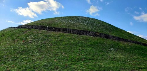 A grassy hill with a stone wall running along its base, under a blue sky with scattered clouds.