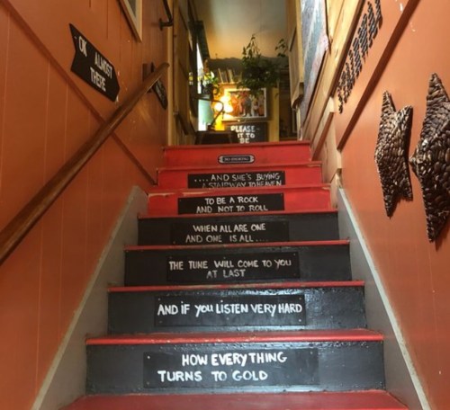 Staircase with painted lyrics and phrases on each step, leading upward in a cozy, artistic setting.