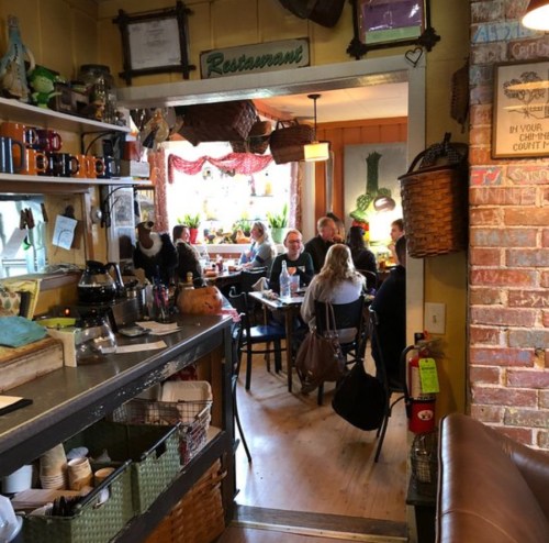 A cozy restaurant interior with diners at tables, colorful decor, and a view of the kitchen area.