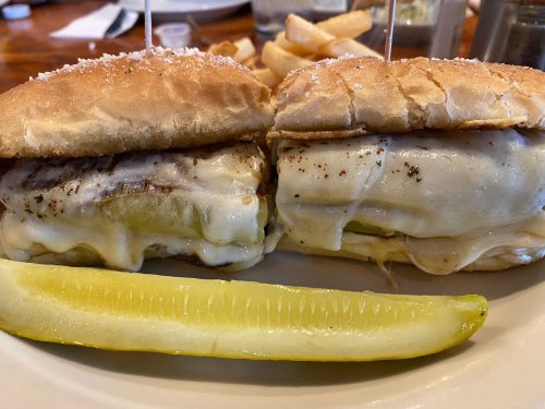 Two cheesy sandwiches with pickles, served with a side of fries and a pickle slice on a white plate.