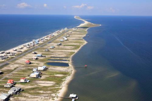 Aerial view of a coastal area with houses along a narrow strip of land bordered by blue water on both sides.
