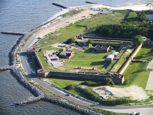 Aerial view of a historic fort surrounded by water, featuring grassy areas and stone walls.