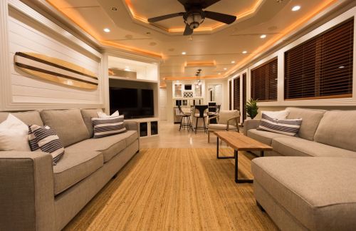 Cozy living room with gray sofas, a wooden coffee table, and warm lighting, featuring a TV and dining area in the background.