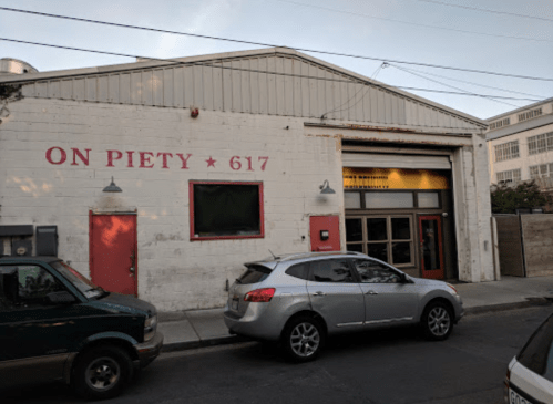 Exterior of a warehouse with "ON PIETY 617" painted on the wall, featuring a large garage door and parked cars.