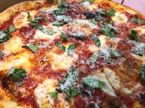 A close-up of a pizza topped with tomato sauce, mozzarella cheese, fresh basil, and grated cheese.