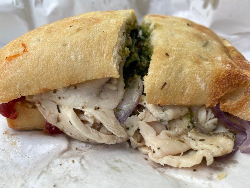 Close-up of a sandwich filled with shredded chicken, herbs, and green sauce, served on a crusty bread roll.