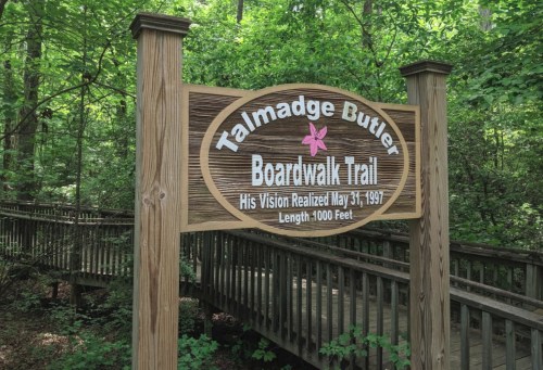 Sign for Talmadge Butler Boardwalk Trail, surrounded by lush greenery, indicating a trail length of 1,000 feet.
