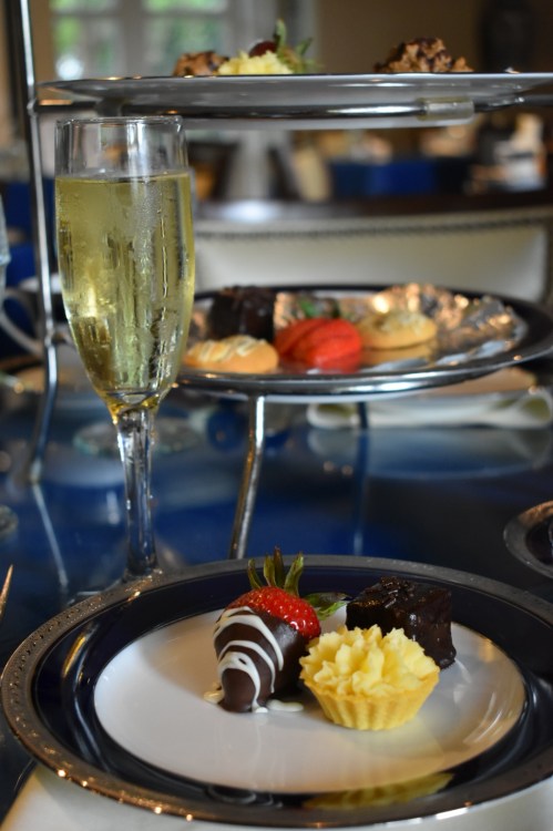 A tiered dessert display with a glass of champagne, featuring chocolate treats, macarons, and a strawberry.
