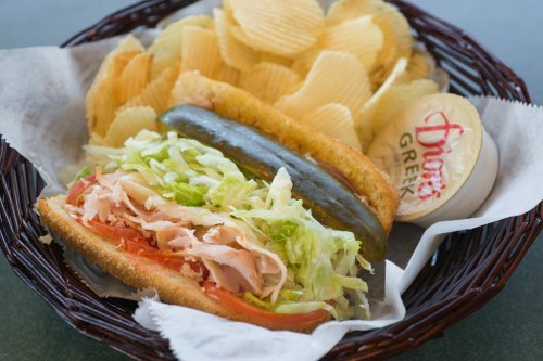 A sandwich with turkey, lettuce, and tomato, served with pickles and potato chips in a basket.