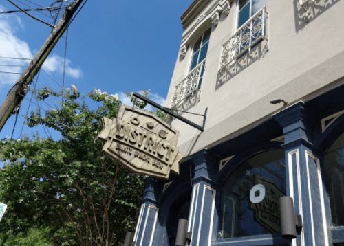 Sign for "District" restaurant hangs from a building with decorative balconies and blue trim under a clear sky.