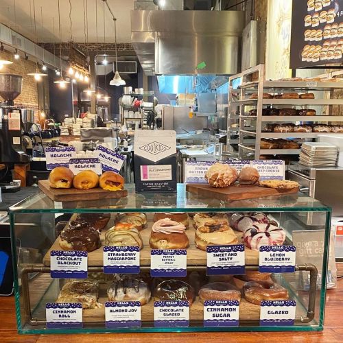 A display case filled with various colorful donuts, labeled with flavors, in a cozy bakery setting.